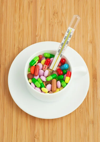 Kopp med mångfärgade tabletter och kapslar och hermometer — Stockfoto
