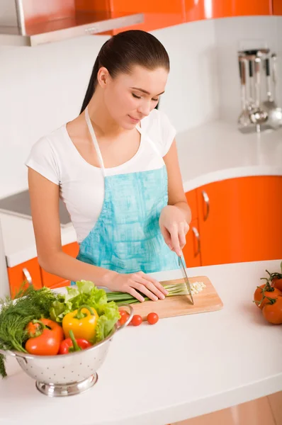Ung kvinna skära grönsaker i ett kök — Stockfoto