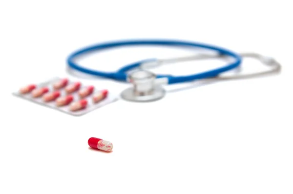 Синий стетоскоп с красными таблетками изолирован — стоковое фото