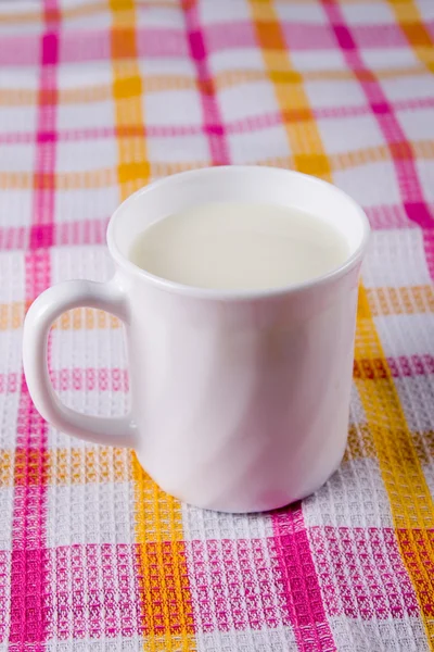 Kareli bir masa örtüsü üzerinde süt bir fincan — Stok fotoğraf