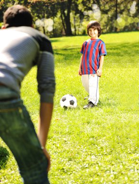 Cute little boy with his father playing with a ball in beautiful park in na clipart