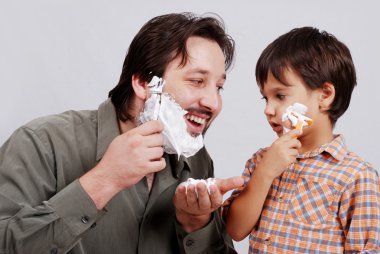 Man in bathroom putting shaving cream on young boy's face clipart