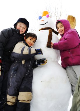 Children playing happily in snow making snowman, winter season clipart