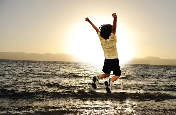 Niño saltando sobre un mar al atardecer —  Fotos de Stock