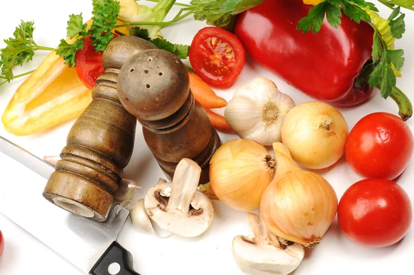 Соль и перцовые шейкеры, овощи, нож на столе — стоковое фото