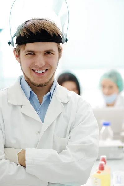 Confident young doctor with mask and folded hands in hospital laboratory — Stock Photo, Image