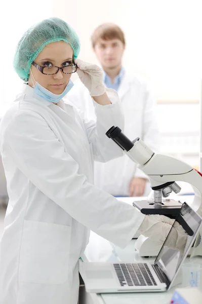 Pretty female researcher using a microscope in a lab — Stock Photo, Image