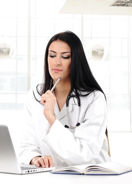 Young woman doctor in white coat at computer thinking — Stock Photo, Image