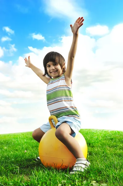 Sportig söta positiva unge, leker glatt med stor boll på grön äng — Stockfoto