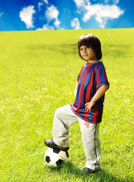 Молодой возбужденный мальчик стоит с мячом в траве на открытом воздухе — стоковое фото
