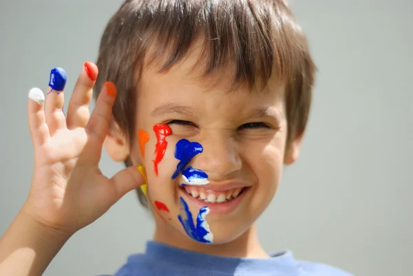 Kid med färg på hans fingrar och ansikte — Stockfoto