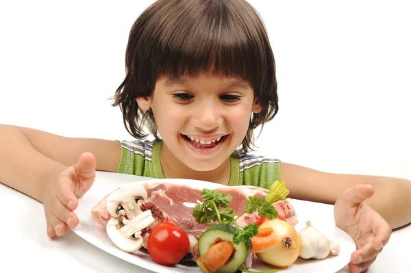 Lindo chico positivo y carne cruda y verduras en plato de lectura para cocinar — Foto de Stock