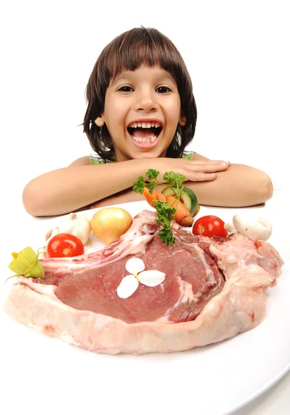 Cute positive boy and raw meat and vegetables in plate reading for cooking — Stock Photo, Image