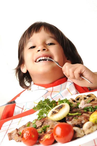 Ładny pozytywny chłopak z widelcem i nożem, jedzenie na stole obiad — Zdjęcie stockowe