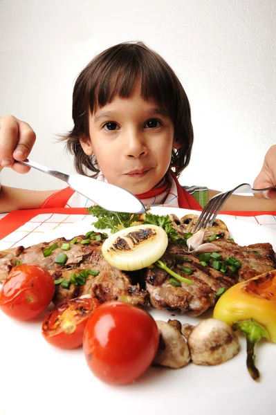 Ładny pozytywny chłopak z widelcem i nożem, jedzenie na stole obiad — Zdjęcie stockowe