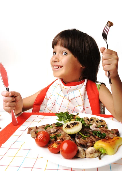 Lindo chico positivo con tenedor y cuchillo comiendo en la mesa del almuerzo — Foto de Stock