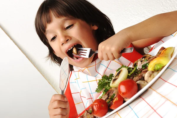 Carino ragazzo positivo con forchetta e coltello mangiare sul tavolo da pranzo — Foto Stock