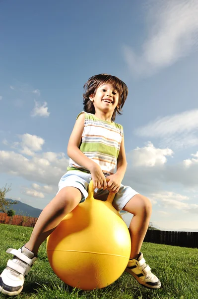 Pequeño niño feliz jugando con la bola grande y saltando con ligero movimiento hacia arriba, s —  Fotos de Stock