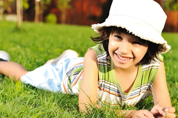 Симпатична дитина з капелюхом на голові лежить на траві в парку — стокове фото