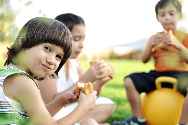Three children in nature playing and eating together — Stock Photo, Image