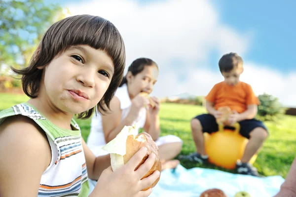 Grupo feliz de crianças ao ar livre no prado: comer e brincar juntos — Fotografia de Stock