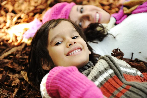 Little happy positive kid laying on fall ground with his mother, yellow and — Stock Photo, Image