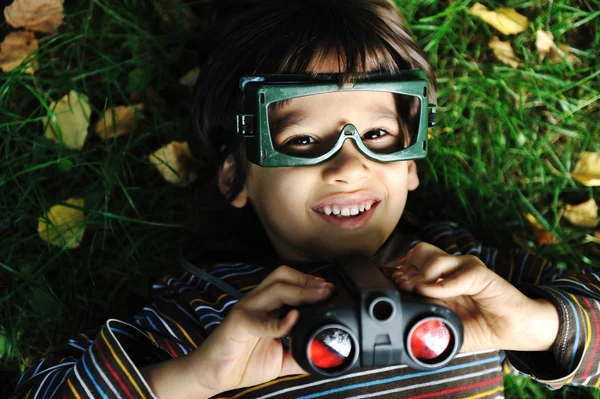 Bonito menino positivo com óculos e binóculos deitado no chão e sorrindo — Fotografia de Stock