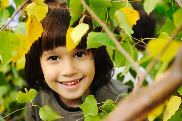 Lycklig barndom utomhus, glada ansikten mellan bladen på träden i för — Stockfoto
