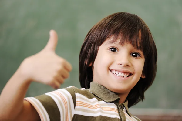 Щасливий хлопчик в класі з великим пальцем вгору: зелена дошка позаду — стокове фото