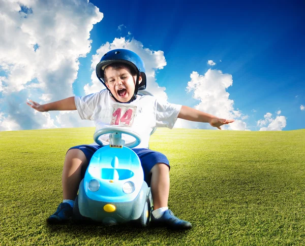 Criança feliz no prado verde dirigindo um carro — Fotografia de Stock