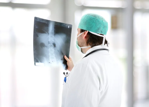 Medical doctor analysing x-ray image handheld, standing at office desk — Stock Photo, Image