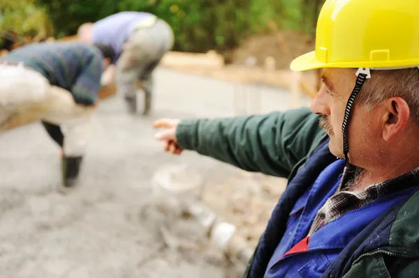Elderly menager on workplace with workers on fresh concrete — Stock Photo, Image