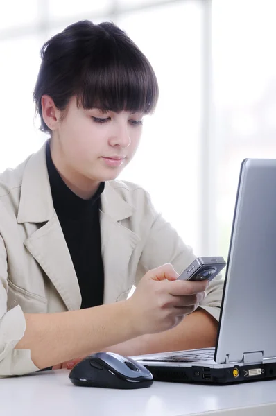 SMS digitando femminile in ufficio, di fronte al computer portatile — Foto Stock