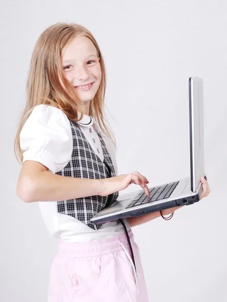 Pequena menina da escola loira jogando na internet de pé com computador portátil — Fotografia de Stock
