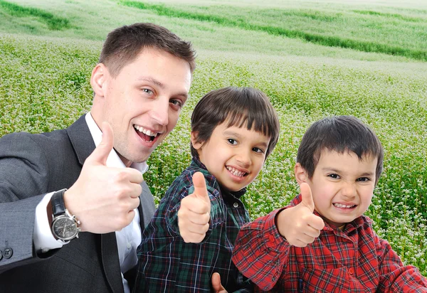 Молодий батько і два сини на відкритому повітрі сидячи і піднімаючись великим пальцем вгору — стокове фото