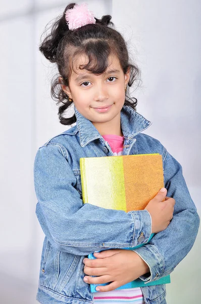 Portrait of a happy little girl standing with notebook against school windo — Stock Photo, Image