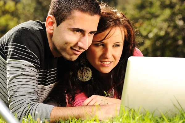 An attractive man and woman couple in the park on laptop computer — Stock Photo, Image