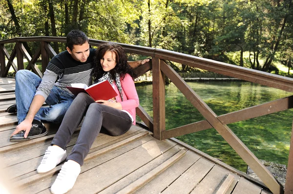 Young couple, girl and boy sitting in park and reading a book — Stock Photo, Image