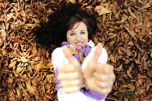 Dívka mladá kráska na podzim pozemní a listy s palce nahoru — Stock fotografie