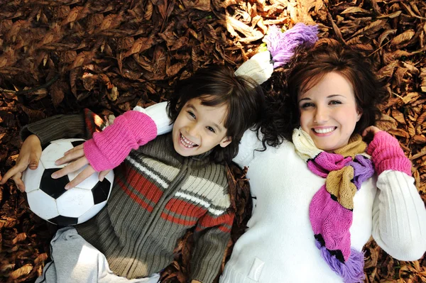 Kleines glückliches positives Kind, das mit seiner Mutter auf dem Boden liegt, gelb und — Stockfoto