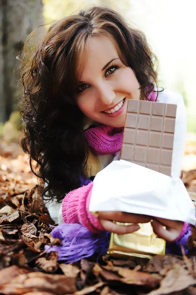Joven chica de belleza comiendo chocolate en la naturaleza, escena de otoño en el suelo —  Fotos de Stock