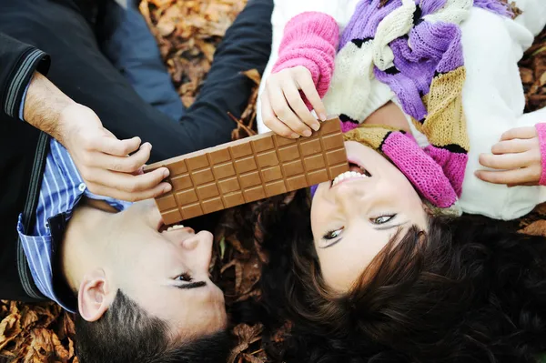 Young beauty girl and her boyfriend eating together chocolate in nature tog — Stock Photo, Image