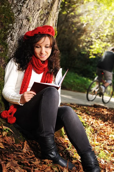 Краса чудова осінь дівчина сидить на природі біля дерева і читає т — стокове фото