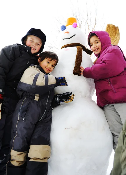 Crianças brincando alegremente na neve fazendo boneco de neve, temporada de inverno — Fotografia de Stock