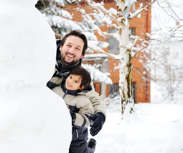 Père et fils jouant heureux dans la neige faisant bonhomme de neige, saison d'hiver Photo De Stock
