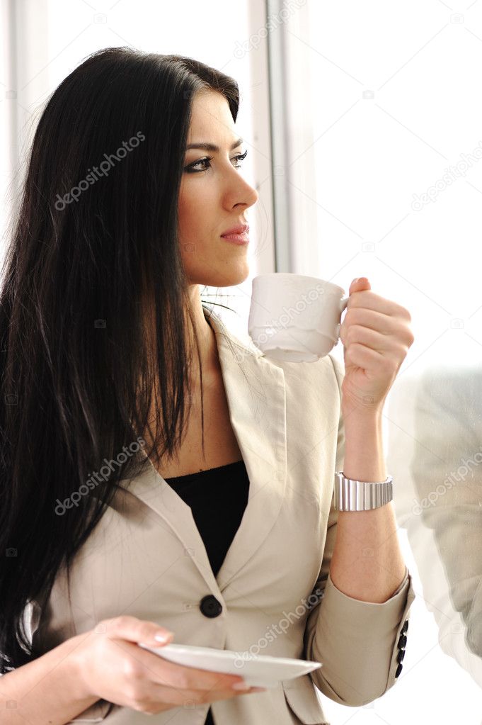 Young pretty woman drinking coffee in office, beside the glass window