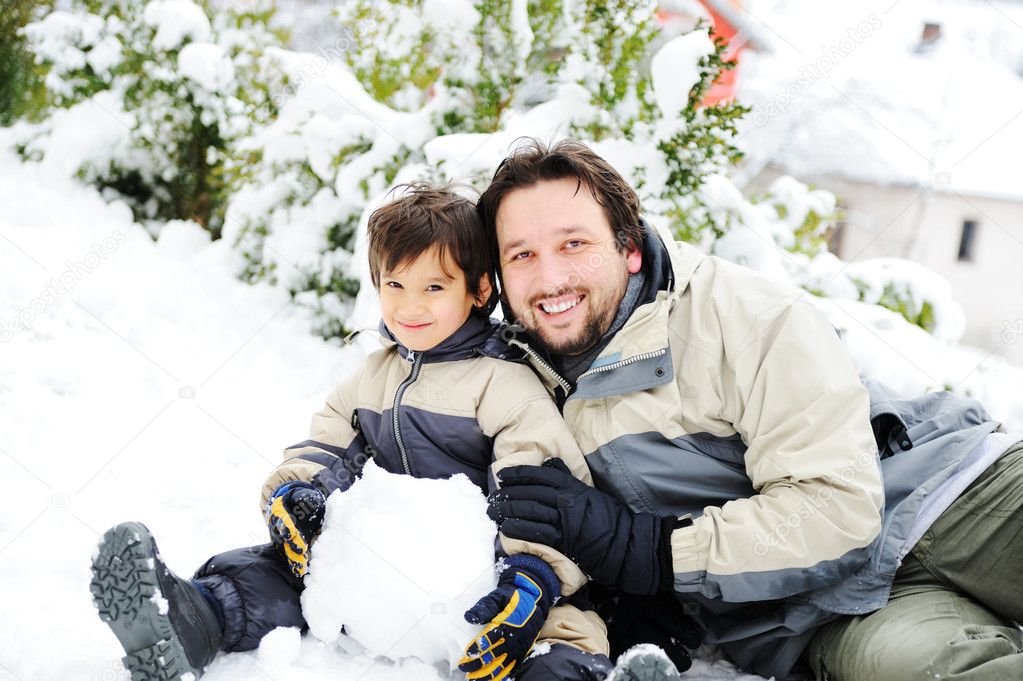 Father and son playing happily in snow making snowman, winter season