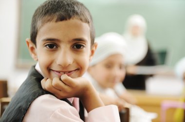 Positive kid in classroom smiling and looking in camera clipart