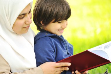 Mother Muslim and her son in the nature, reading together clipart