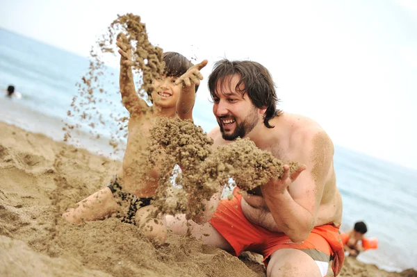 Jugando juntos en la arena en la playa, padre joven y un hijo pequeño —  Fotos de Stock